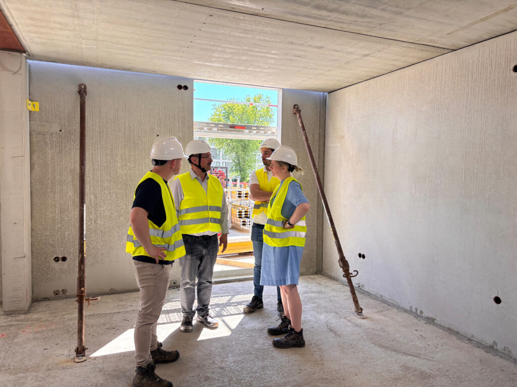 Mehrere Personen mit Helmen und Warnwesten besprechen den aktuellen Baufortschritt in einem Rohbauraum.